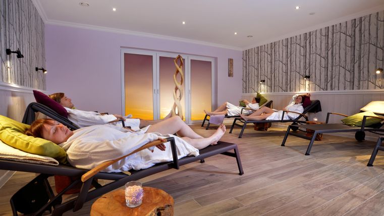 Ein entspannender Wellnessraum mit Liegen und beruhigenden Farben. Mehrere Personen genießen eine Auszeit in bequemen Bademänteln.