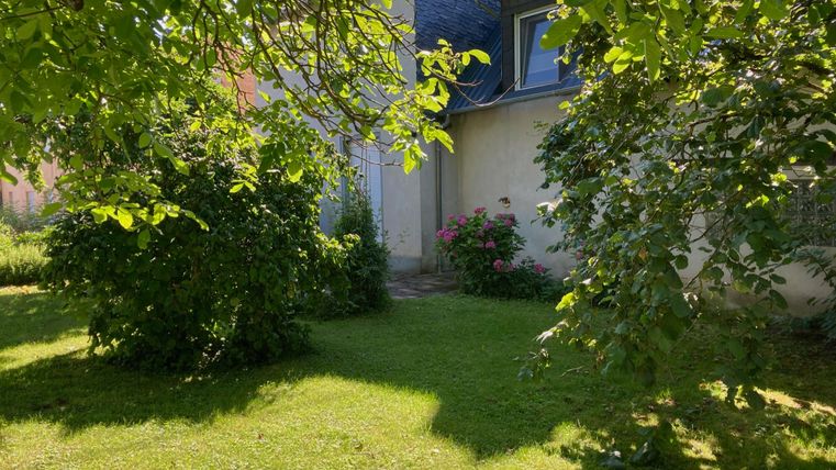Ein grüner Garten mit Bäumen und Blumen. Im Hintergrund ist ein Haus zu sehen.