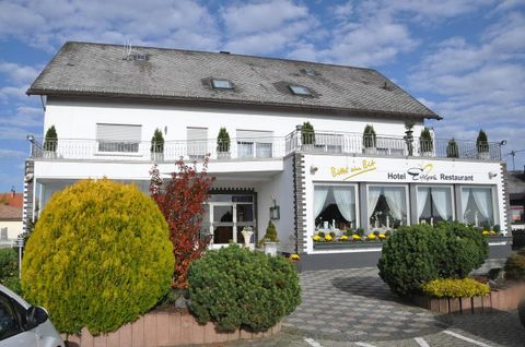 Ein charmantes Hotel mit einem einladenden Restaurant. Die Fassade ist freundlich gestaltet und von gepflegten Pflanzen umgeben.