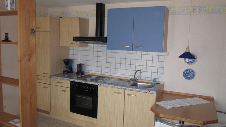 Eine moderne Küche mit Holzschränken und blauen Fronten. Der Raum ist hell und gut ausgestattet mit Herd, Spüle und Kaffeemaschine.