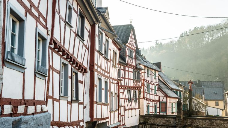 Einmalige Fachwerkhäuser mit rot-weißen Fassaden in einer malerischen Umgebung. Die Häuser sind entlang einer kleinen Straße angeordnet, umgeben von sanften Hügeln.