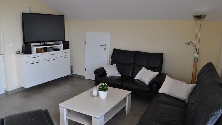 Ein modernes Wohnzimmer mit schwarzen Ledersofas und einem flachen Fernseher an der Wand. Der Tisch ist schlicht und dekoriert mit einer kleinen Pflanze.