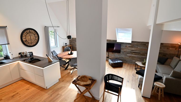 Eine moderne, helle Innenansicht mit einer offenen Küche und einem Wohnbereich. Der Raum ist elegant mit Holzfußboden und geschmackvoller Einrichtung gestaltet.