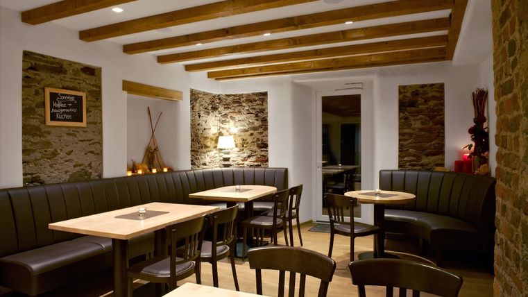 Ein gemütliches Restaurant mit Holzbalkendecke und warmem Licht. Die Einrichtung besteht aus modernen Tischen und Bänken aus Holz.