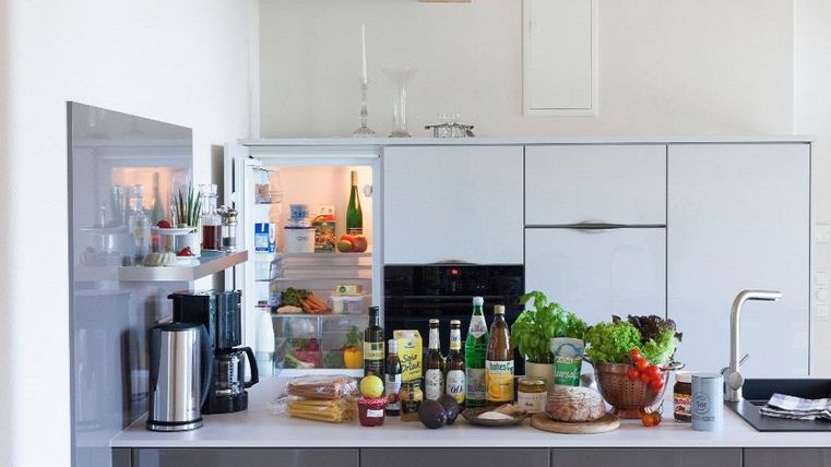 Une cuisine moderne avec une variété d'aliments sur le plan de travail. Le réfrigérateur est partiellement ouvert et contient des fruits et légumes frais.