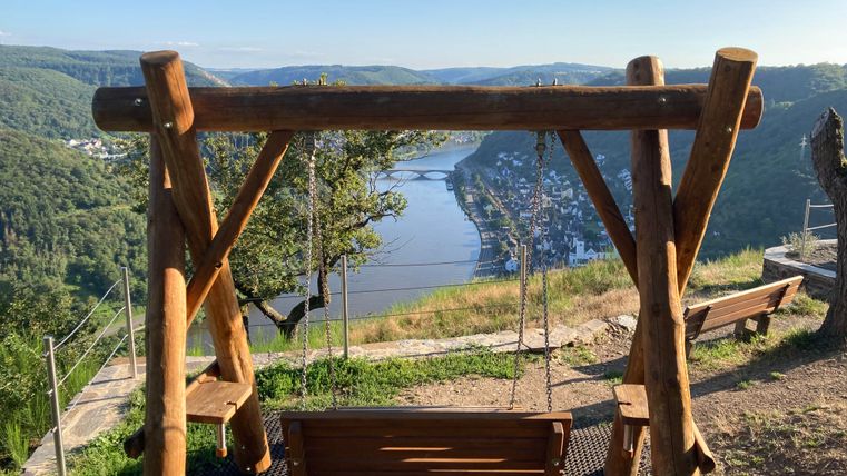 Eine Holzschaukel mit Blick auf einen Fluss und die umliegende Landschaft. Die Szene vermittelt Ruhe und Naturverbundenheit.