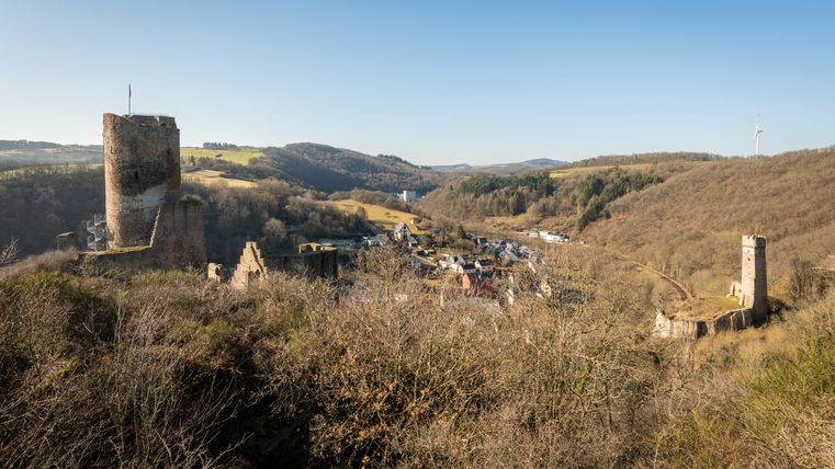 Ruinen der Monrealer Burgen in einer hügeligen Landschaft mit blauem Himmel.