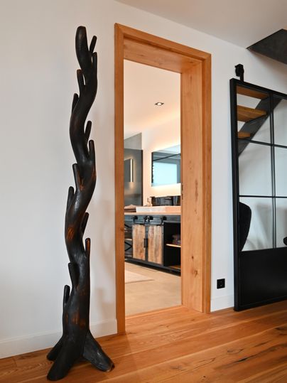 Eine moderne Wohnung mit einem stilvollen, dunklen Holzstander und einem offenen Zugang zur Küche. Der Boden ist aus hellem Holz, was eine gemütliche Atmosphäre schafft.