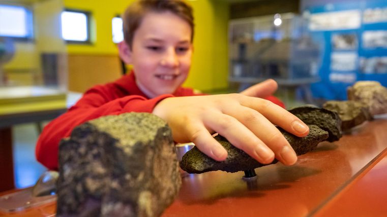 Ein Junge erkundet Steine in einem Museum. Er berührt die Objekte mit Interesse und Freude.