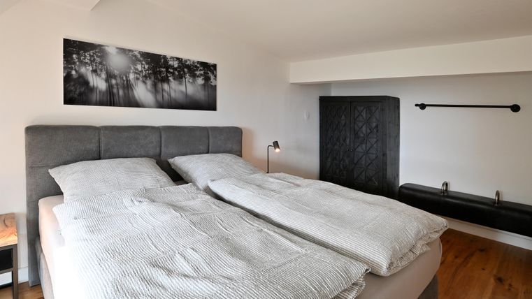 Ein modernes Schlafzimmer mit einem Doppelbett und gestreiften Bettdecken. An der Wand hängt ein Schwarz-Weiß-Bild von Bäumen.