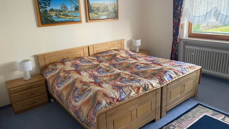 Ein gemütliches Schlafzimmer mit einem großen Doppelbett und Holzmöbeln. An der Wand hängen zwei Bilder, und das Fenster lässt natürliches Licht herein.