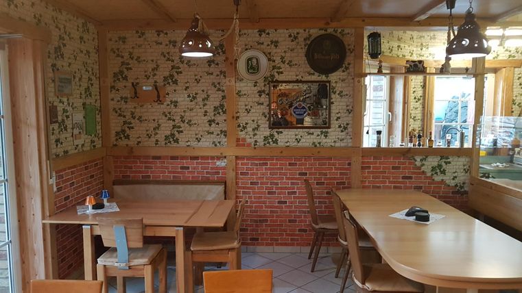 Ein gemütlicher Essbereich mit Holztischen und Stühlen. Die Wände sind mit floralem Muster und Backsteinoptik dekoriert.