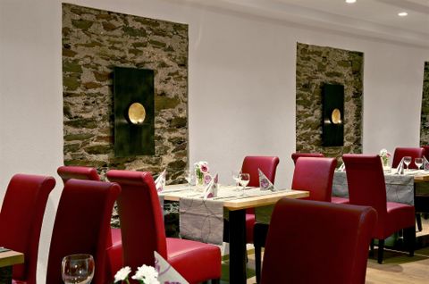 Ein modernes Restaurant mit roten Stühlen und Holztischen. Die Wände sind mit Steinen dekoriert und es gibt eine stilvolle Beleuchtung.