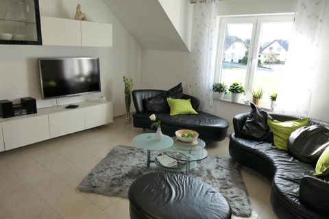 Een moderne woonkamer met elegante zwarte meubels en groene accenten. Grote ramen zorgen voor veel natuurlijk licht en verbinden de binnenruimte met de buitenwereld.