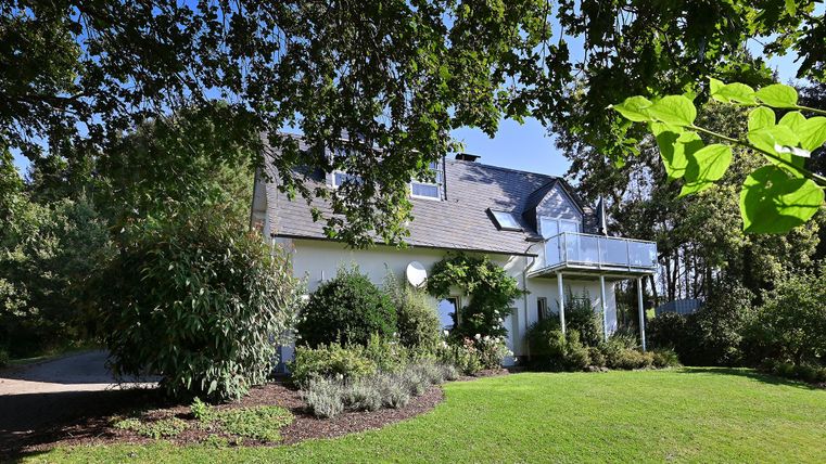 Ein schönes Haus umgeben von Grün und Bäumen. Der Garten ist gepflegt mit einer Rasenfläche und verschiedenen Pflanzen.