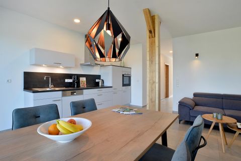 Eine moderne Küche mit einem Esstisch und bunten Früchten. Im Hintergrund sind ein gemütliches Sofa und stilvolle Lampen zu sehen.