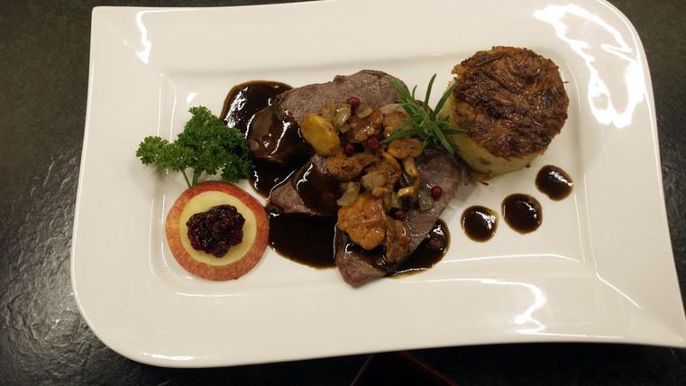 Ein elegantes Gericht mit zartem Fleisch, begleitet von einer dunklen Sauce. Dazu gibt es eine Portion Kartoffelgratin und eine Dekoration aus frischen Kräutern.