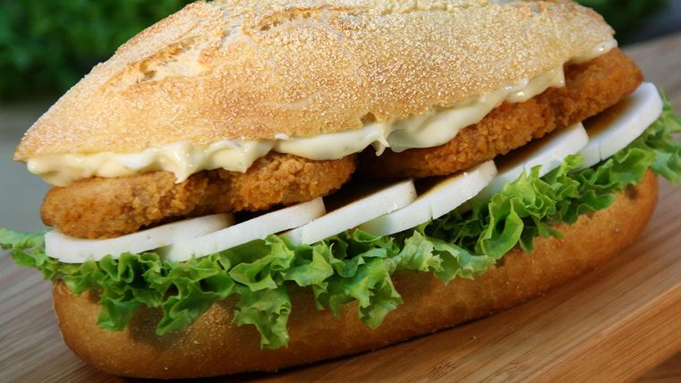 Ein saftiges Sandwich mit knusprigen Chicken Nuggets, frischem Salat und Zwiebeln. Serviert auf einem weichen Brötchen mit etwas Mayonnaise.