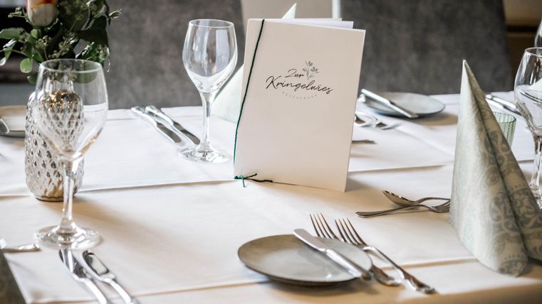 Ein elegant gedeckter Tisch mit Besteck, Gläsern und einer Menükarte. Die Tischdekoration vermittelt eine festliche Atmosphäre.