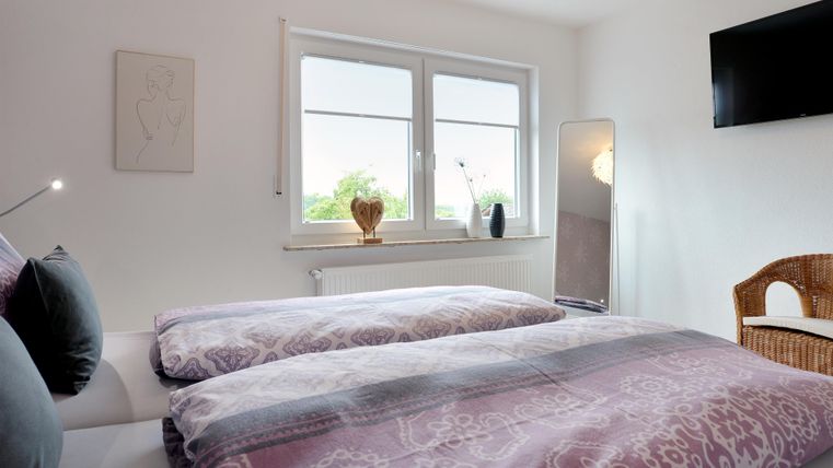 Ein gemütliches Schlafzimmer mit einem Doppelbett und modernen Dekorationen. Großzügige Fenster sorgen für viel Tageslicht und eine einladende Atmosphäre.