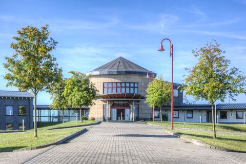 Ein modernes Gebäude mit einem runden Dach und großen Fenstern. Grüne Bäume säumen den Weg, der zum Eingang führt.