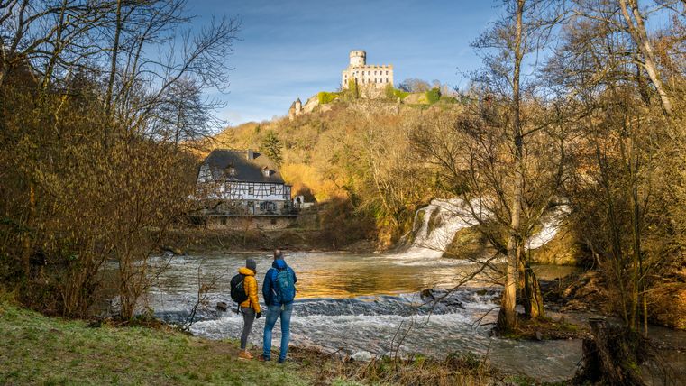 Zwei Personen stehen am Ufer des Elzbachs mit Blick auf die Pyrmonter Mühle und Burg Pyrmont.