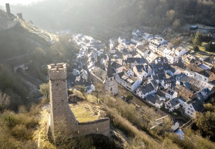 Luftaufnahme von Monreal mit einer Burg im Vordergrund und Fachwerkhäusern im Tal. Die Landschaft ist von Bäumen und Hügeln umgeben., © Eifel Tourismus GmbH, D. Ketz