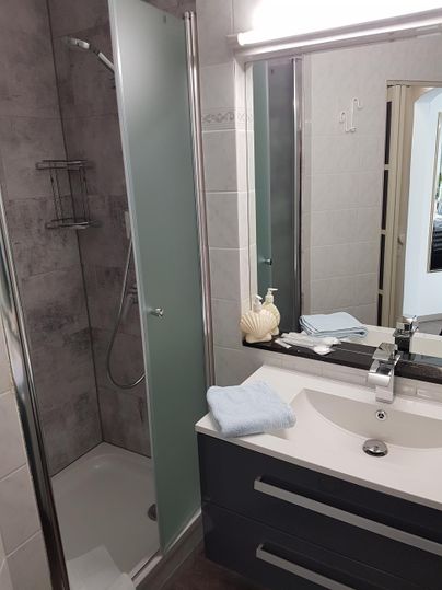 Ein modernes Badezimmer mit einer Dusche und einem Waschbecken. Der Raum ist einfach und sauber eingerichtet.