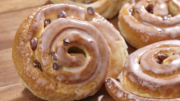 Zimtrollen mit einer glasierten Oberfläche und Schokoladenstückchen. Sie liegen auf einem Holzbrett.