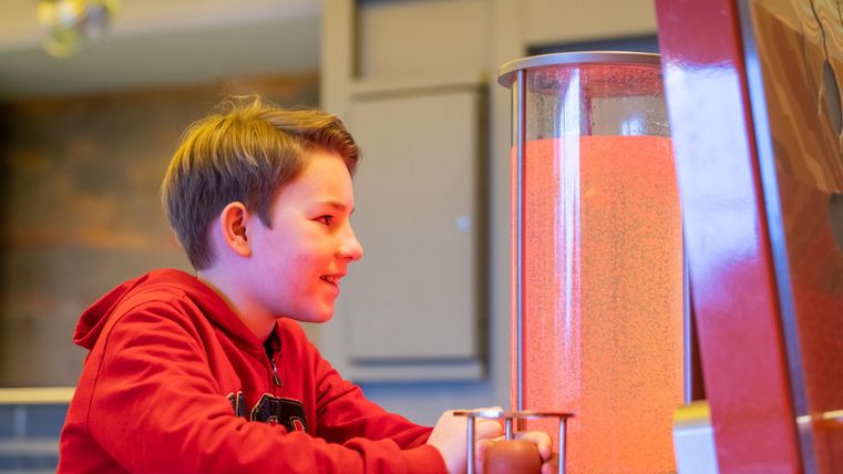 Ein Junge sitzt vor einem interaktiven Gerät und beobachtet fasziniert die bunten Lichter. Er trägt einen roten Hoodie und schaut konzentriert.