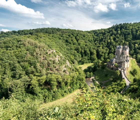 Burg Eltz thront majestätisch auf einem bewaldeten Hügel, umgeben von üppiger grüner Landschaft und blauem Himmel., © Rheinland-Pfalz Tourismus GmbH, D. Ketz