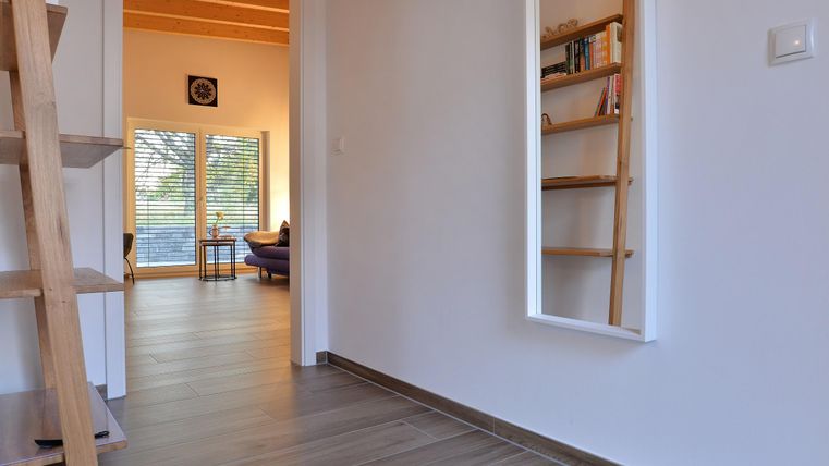 Ein heller Flur mit Holzregalen und einem Spiegel. Im Hintergrund sieht man ein Wohnzimmer mit großen Fenstern.
