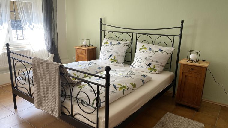 Ein gemütliches Schlafzimmer mit einem Doppelbett und hellen Bettwaren. Die Wände sind in einem sanften Grünton und es gibt dekorative Nachttische.