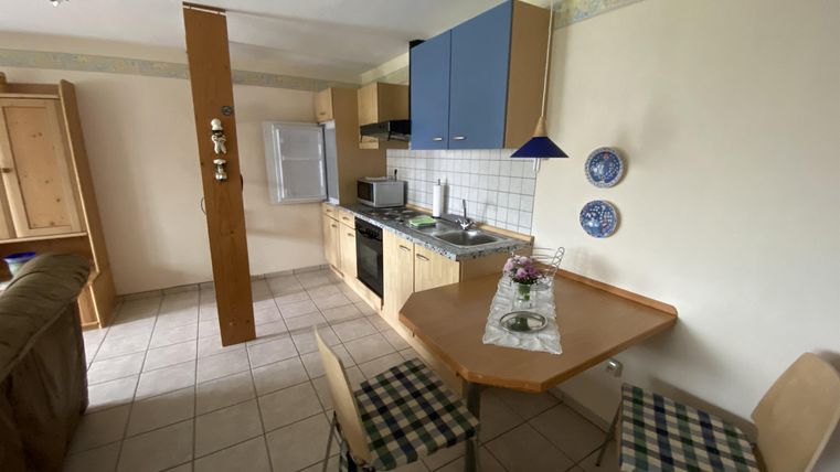 Eine kleine, gemütliche Küche mit Holzschränken und einer Essecke. Es gibt einen Kühlschrank und eine Kochzeile mit blauen Schränken.