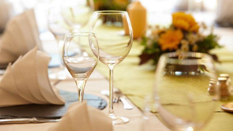Ein eleganter Tisch mit hübsch gefalteten Servietten und Gläsern. Im Hintergrund sind Blumenarrangements zu sehen, die eine festliche Atmosphäre schaffen.