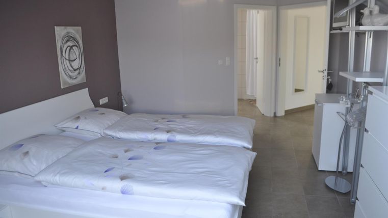 Ein einfaches, helles Schlafzimmer mit zwei Einzelbetten und modernen Möbeln. Die Wände sind in neutralen Farben gehalten, und es gibt einen Zugang zu einem Badezimmer.