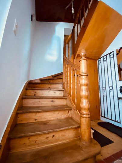 Eine Holztreppe mit einem geschwungenen Geländer führt nach oben. Der Bereich ist hell und freundlich, mit einer weißen Wand und einem Sockel.