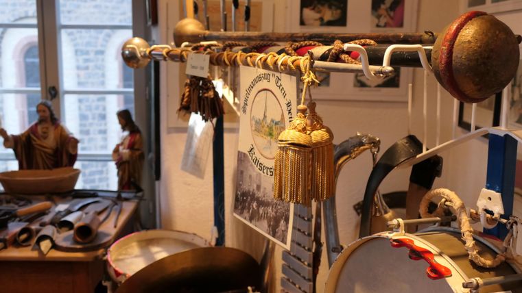 Eine Reihe von musikinstrumenten hängt an einem Ständer, darunter Trommeln und Rasseln. Der Hintergrund zeigt Fotos und kleine Statuetten.