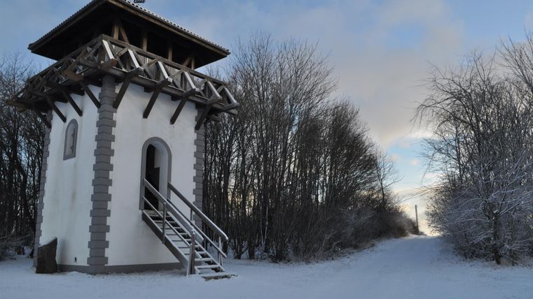Ein Schneestand mit einem weißen Aussichtsturm und einer Treppe. Umgeben von schneebedeckten Bäumen und einem klaren Himmel.