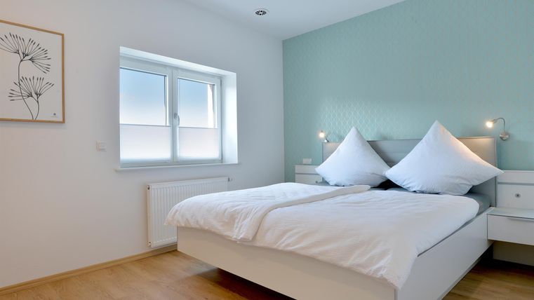 Ein modernes Schlafzimmer mit einem großen Doppelbett und zwei Kissen. Die Wände sind in sanften Farben gehalten und es gibt ein Fenster, das Tageslicht hereinlässt.