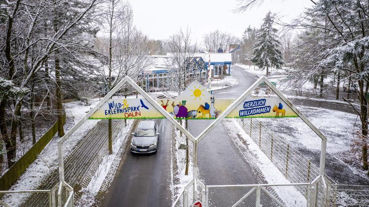 Ein Eingang zu einem Freizeitpark im Schnee. Begrüßungsschild und ein Auto sind sichtbar.