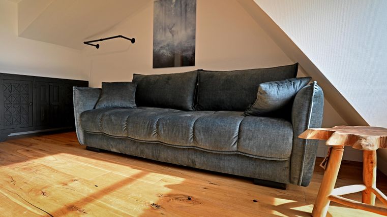 Ein gemütliches, graues Sofa steht in einem hellen Raum mit Holzboden. An der Wand hängt ein dunkles Bild über dem Sofa.