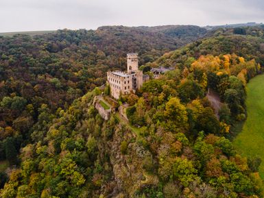 Burg Pyrmont auf einem steilen Felsen, umgeben von herbstlich gefärbtem Wald und weiter Hügellandschaft.