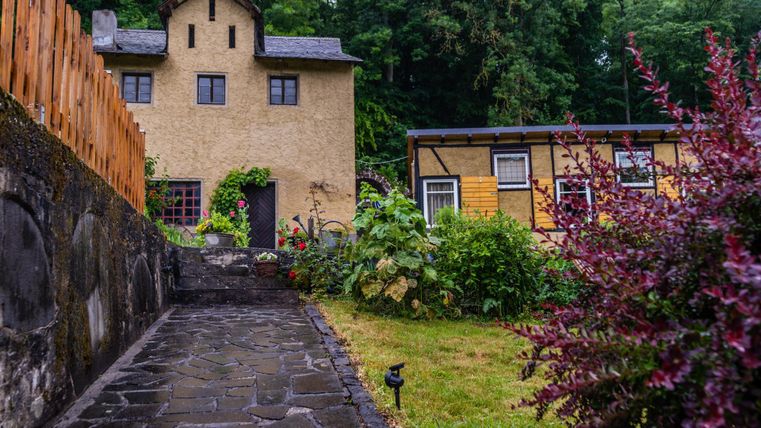Une maison charmante avec une façade rustique et un jardin bien entretenu. Au premier plan, un chemin en pierre mène à la porte d'entrée.