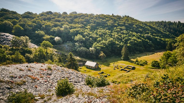 Blick auf die Herrenwiese und das neu gebaute Spalthaus. Links ist viel Schiefer zu sehen und im Hintergrund eine Waldlandschaft.