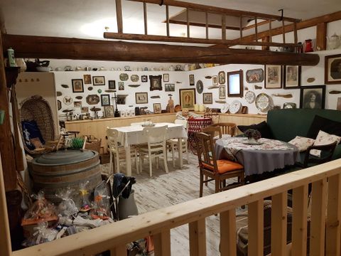 Ein gemütlicher Raum mit Holzmöbeln und zahlreichen Kunstwerken an der Wand. Der Tisch ist festlich gedeckt, und es gibt einige Gegenstände auf dem Boden.