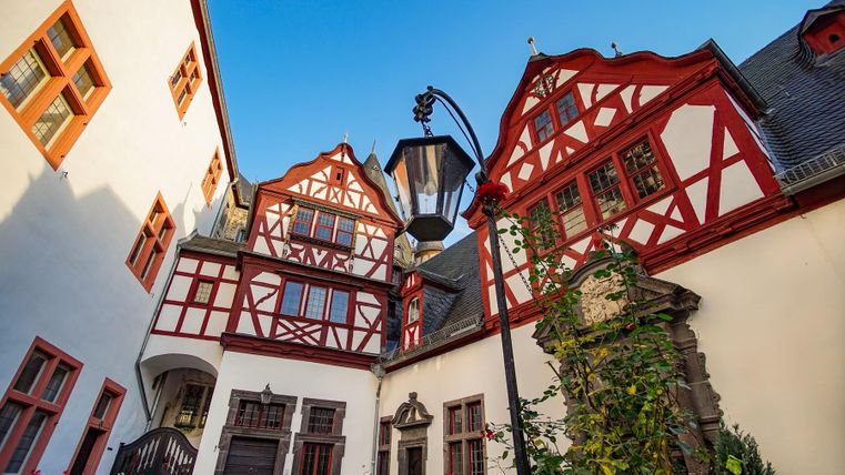 Ein malerischer Innenhof mit Fachwerkhäusern und blühenden Blumen. Die Architektur hat rot-weiße Akzente und ein gemütliches Flair.