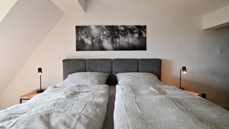 Ein modernes Schlafzimmer mit zwei Betten und eleganter Bettwäsche. An der Wand hängt ein Schwarz-Weiß-Bild von einem Wald.