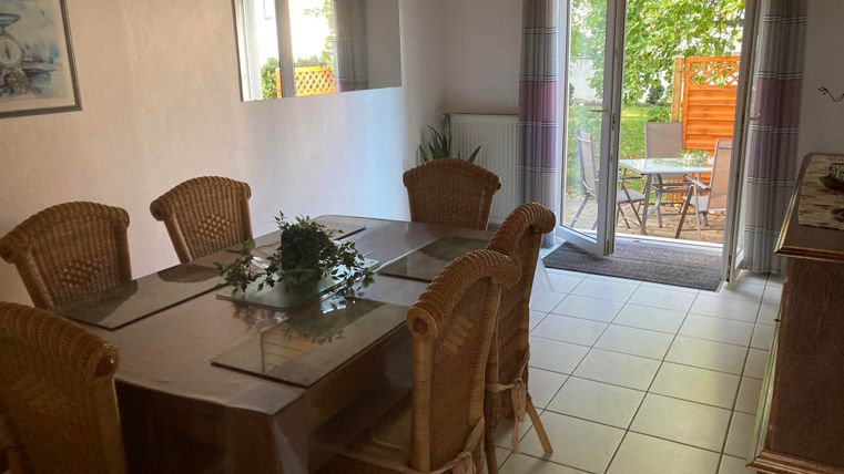 Ein heller Essbereich mit einem großen Tisch und geflochtenen Stühlen. Die Türen führen zu einer gemütlichen Terrasse mit Blick ins Grüne.