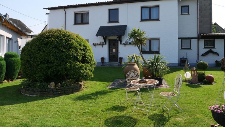 Een mooi huis met een verzorgde tuin. Er is een gezellige zithoek met een tafel en witte stoelen.